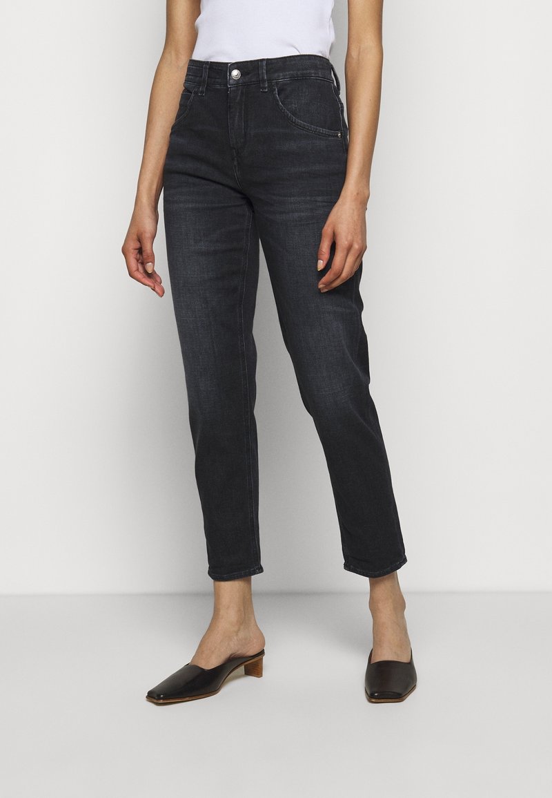 Jeans in denim scuro con una vestibilità classica, dotati di cinque tasche, una tasca anteriore piccola e un lavaggio sottile. Abbinati a mule nere su uno sfondo neutro.