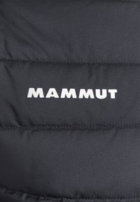 Tejido negro acolchado con el logo blanco "MAMMUT" impreso en él, probablemente parte de una chaqueta o equipo para actividades al aire libre.