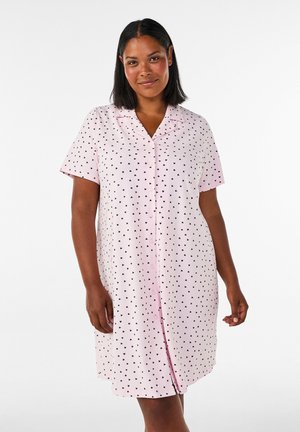 Vrouw met stijl zwart haar die een lichtroze korte mouw knoopjurk draagt met een kleine zwarte hartprint.
