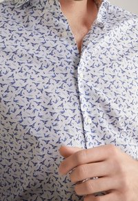 Wit overhemd met knopen voor en een blauw vogelpatroon. Voorzien van een klassieke kraag, lichtgewicht stof en gestikte knopen.