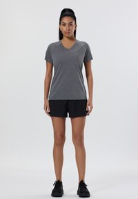T-shirt de sport gris à col en V assorti à un short noir, tous deux en tissu léger. Des chaussures de sport noires complètent la tenue.