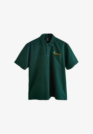 Groene korte mouwen shirt van stof met een kraag, voorzien van een gele geborduurde Guinness-logo en een zak aan de linkerkant.