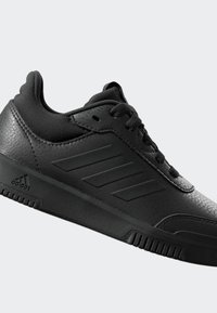 Chaussure de sport noire avec une tige en cuir texturé, des accents en maille et trois bandes parallèles sur le côté. Semelle en caoutchouc avec une adhérence à stries.