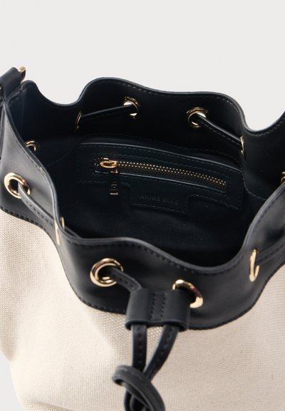Beige stoffen bucketbag met zwarte leren bovenrand, gouden ringen, trekkoordsluiting en binnenzak met rits.