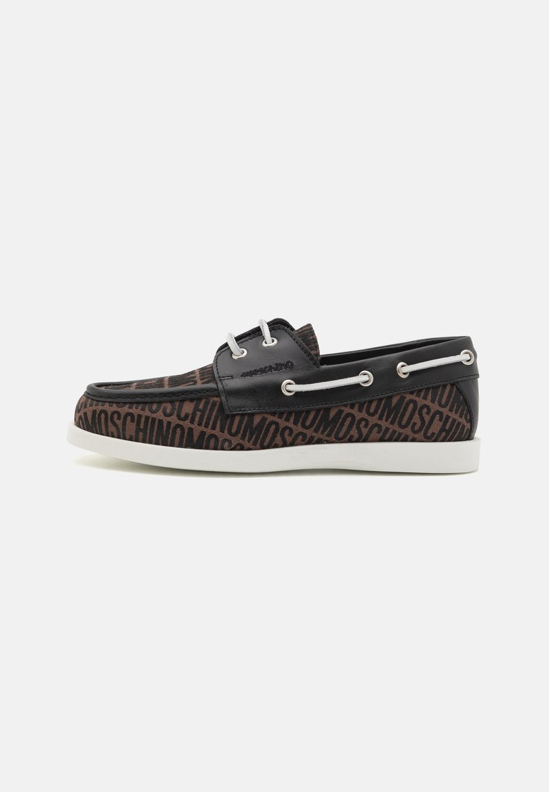 Zapato de patrón negro y marrón con logotipo visible, parte superior de cuero, diseño tipo barco, suela de goma blanca y ojales metálicos.