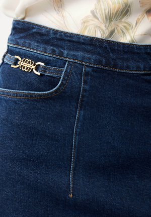 Dunkelblauer Jeansrock mit goldener dekorativer Schnalle an der Seitentasche, kombiniert mit einem hellfarbenen, geblümten Oberteil, das hineingesteckt ist.