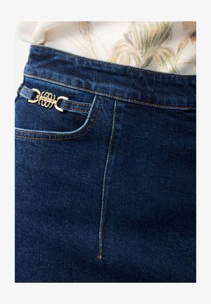 Dunkelblauer Jeansrock mit goldener dekorativer Schnalle an der Seitentasche, kombiniert mit einem hellfarbenen, geblümten Oberteil, das hineingesteckt ist.