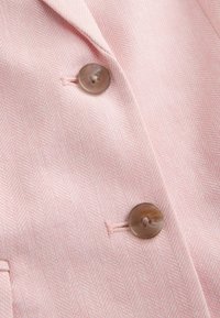 Gros plan sur un tissu chevrons rose clair avec deux boutons ronds marron cousus dans des boutonnières sur un vêtement.