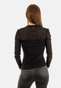 Top negro de manga larga con hombros de malla transparente, diseño ajustado y textura suave, combinado con jeans de mezclilla oscuros que tienen bolsillos traseros.