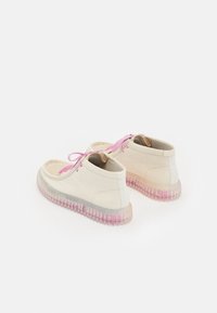 Chaussures de couleur claire avec une surface texturée, des lacets roses et des semelles transparentes présentant un dégradé du transparent au rose. Design à tige basse.