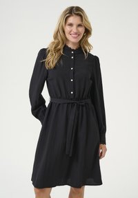 Černé šaty na knoflíky vyrobené z lehk�ého materiálu, s páskem na uvázání, elastickými manžetami s krajkovým lemem a skládánou sukní.