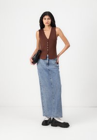 Haut sans manches marron avec un décolleté en V profond et des boutons sur le devant, associé à une longue jupe en denim bleu et des chaussures à plateforme noires.