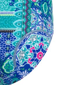 Um tecido multicolorido apresenta padrões intrincados em turquesa, azul, rosa e branco, com diversas formas geométricas e acentos decorativos.