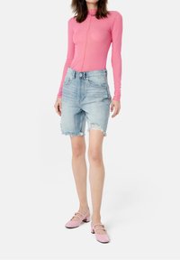 Long-sleeve pink top with front seam, distressed light blue denim shorts, and pink Mary Jane shoes with small flower accents.