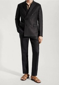 Męski ciemnoszary, podwójnie zapinany garnitur o teksturowanym wykończeniu, dopasowany krój, w połączeniu z brązowymi sandałami na paski.