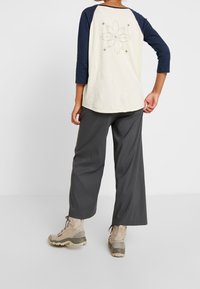 Krämmig t-shirt med trekvartsärmar och marinblå ärmar, med en blommig design på baksidan. Bärs med löst sittande grå byxor och bruna stövlar.