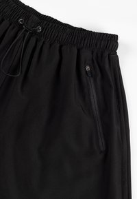 Czarne sportowe szorty z elastycznym pasem, regulowanym sznurkiem i kieszenią na zamek z boku do bezpiecznego przechowywania. Gładka faktura.