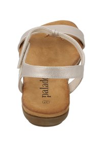 Sandalias de cuero beige con diseño de tira cruzada, plantilla acolchada en tono marrón y suela baja de goma marrón. Presentan un aspecto minimalista y limpio.