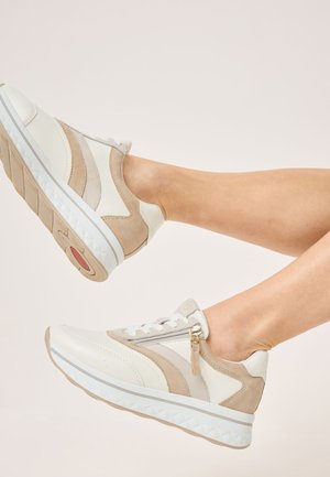 Zapatillas beige y blancas con un diseño texturizado y en capas, que cuentan con una cremallera lateral, cordones blancos y una suela acolchada con un dibujo en la parte inferior.