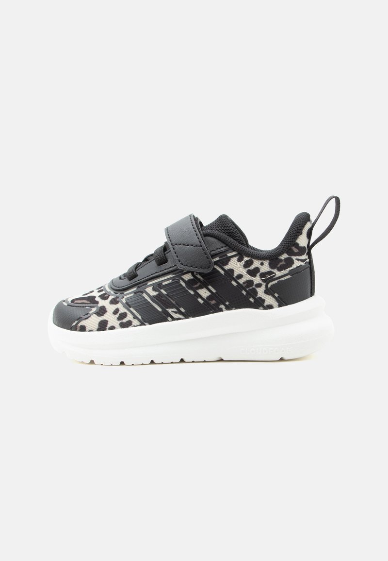 Baskets pour enfants en noir et blanc avec motif animalier, bride à velcro, lacets noirs et semelle épaisse blanche sur fond blanc.