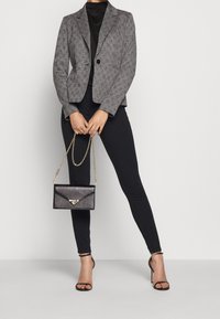 Blazer de cuadros gris con un botón, combinado con pantalones ajustados negros y un bolso de mano negro con cadena, que presenta una textura brillante.