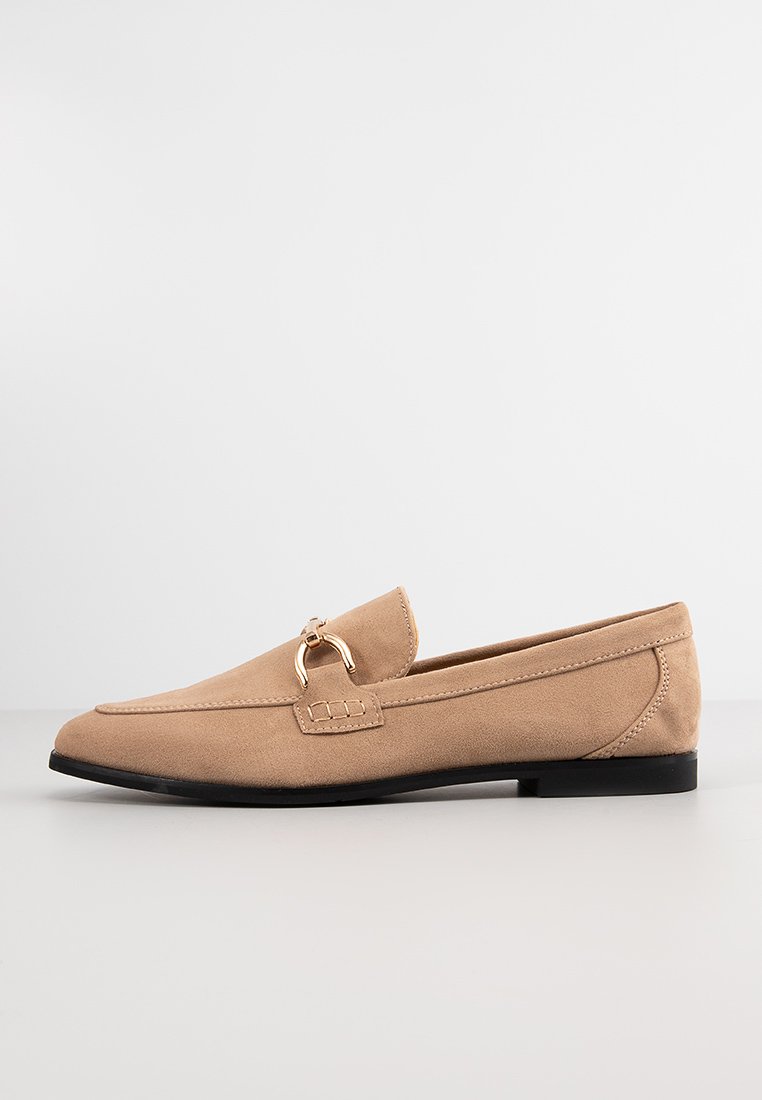 Helle Wildleder-Loafers mit einem goldfarbenen Pferdebit-Detail, flacher schwarzer Sohle und minimalistischem Design, das klare Linien und eine glatte Textur zeigt.