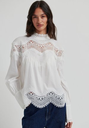 White blouse featuring a high lace neckline and intricately patterned lace trim along the sleeves and bottom hem. Soft, textured fabric.