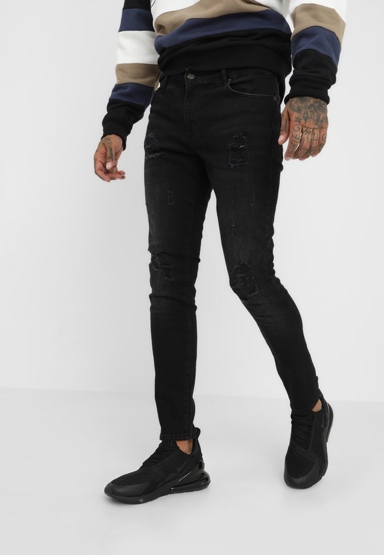 Svarta slitna skinny jeans med fransade detaljer, med en klassisk femfickedesign och minimal stretch, matchade med svarta sportskor.