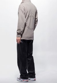 Světlé šedé tričko s vysokým límcem a grafickým nápisem vzadu. Kombinováno s volnými černými koženými kalhotami a bílými sportovními botami.