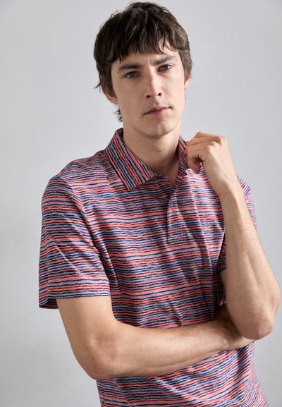Tricou polo cu dungi în roșu, albastru și alb, având guler și mâneci scurte. Material moale cu un model texturat, ondulat.