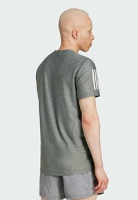 Camiseta deportiva gris de manga corta con cuello redondo, que presenta tres rayas blancas en la manga izquierda. Tejido suave y ligero.