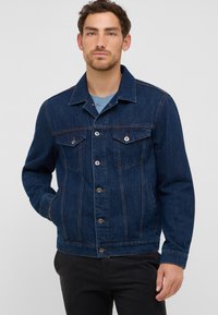 Ciemnoniebieska kurtka dżinsowa z klasycznym kołnierzem, z przodu zapinana na guziki, z dwiema kieszeniami na piersi i kieszeniami bocznymi. Posiada akcenty w postaci przeszyć oraz luźny krój.