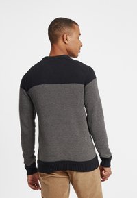 Pull tricotat cu un design bi-color, cu o secțiune superioară de culoare albastru închis și o secțiune inferioară texturată de culoare gri deschis. Manșete și tiv cu model îndoială.
