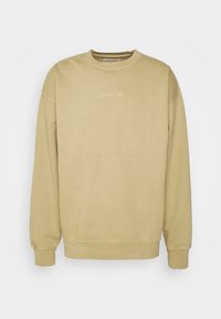 Sudadera beige con cuello redondo, mangas largas y puños de canalé. Presenta un pequeño bordado "REVOLUTION" en el pecho. Textura suave.
