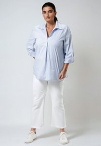 Chemise à rayures bleu clair, à boutons, avec un col évasé et des manches mi-longues, portée avec un pantalon blanc court et des baskets blanches.