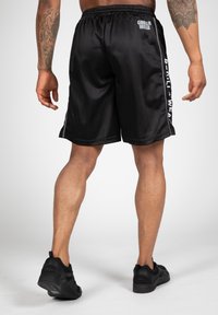 Zwarte sportshorts met een elastische tailleband, voorzien van een gladde textuur en witte logodetails aan de zijkanten. Draag ze met zwarte sneakers.