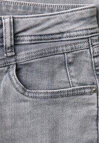 Close-up van grijze spijkerbroek die een voorzak, riemlus en gedetailleerd stiksel toont.