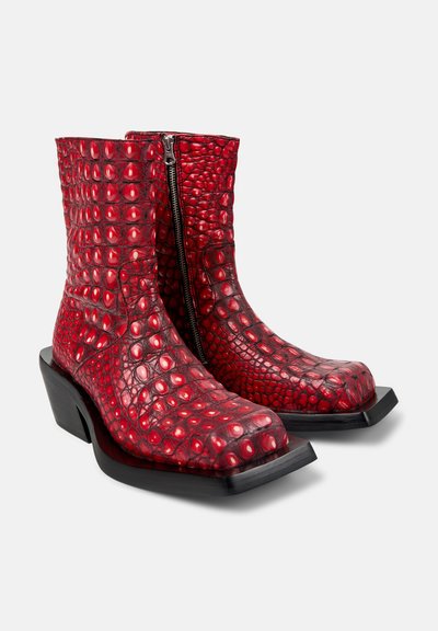 Bottes cheville en cuir rouge à texture crocodile avec bouts carrés, talons noirs angulaires et fermetures éclair latérales sur fond blanc.