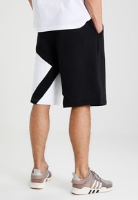 Black and white athletic shorts feature a geometric design, made from a smooth fabric. Worn with light-colored sneakers.