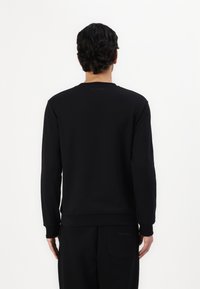 Black sweatshirt with long sleeves, round neckline, ribbed cuffs, and hem. Features a subtle logo printed on the back near the collar.