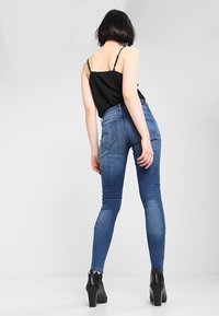 Jeans de denim azul ajustados con un lavado medio, con bolsillos traseros y una textura suave, combinados con una camiseta sin mangas negra y botas de tobillo.