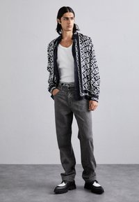 Μαύρο και λευκό πουκάμισο με σχέδια, λευκή αμάνικη μπλούζα, γκρι τζιν και μαύρα παπούτσια με ασημένιες λεπτομέρειες. Υφασμάτινη υφή και μοντέρνος σχεδιασμός.