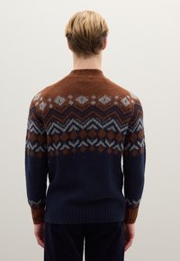 Gestrickter Pullover mit geometrischem Muster in Braun-, Grau- und Marineblau-Tönen. Flauschige Textur und ein geripptes Bündchen vervollständigen das Design.