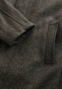 Mörkgrå yllekappa med texturerat fiskbensmönster, skräddarsydd krage och en sidoficka, vilket framhäver en förfinad finish.