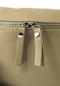 Beige leren tas met een gestructureerd oppervlak, voorzien van een zilverkleurige ritssluiting, twee leren trekker en kenmerkende metalen hardware details.