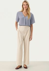 Light blue short-sleeve blouse with a v-neck, paired with wide-leg beige pants. Burgundy flats complete the look. Smooth fabric texture.