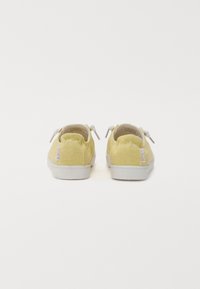 Baskets en toile jaune avec semelles et lacets blancs. Présentent une tige texturée et un petit logo sur le talon. Vue arrière.