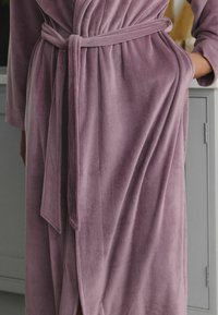 Lilla korduroy hommikumantel, millel on sidumisvöö, pehme tekstuur ja pikad varrukad. Kangas on vertikaalsete soontega.