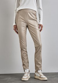 Beige neplederen broek met een slim fit, zijritsen en een gladde textuur, gecombineerd met beige en witte high-top sneakers.