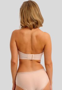 Beige strapless beha met golvende randen en haak-en-oogsluiting, gecombineerd met bijpassende hooggewaisted onderbroek. Een gladde textuur en een minimalistisch ontwerp.